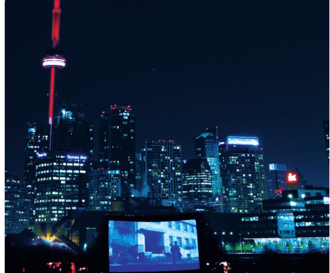 Toronto skyline at dusk with the CN Tower lit red, a Local 416 Family Movie Night screen glowing on the lawn below